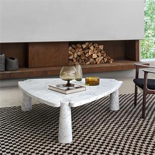 Pale stone coffee table with a rounded triangular top and tapered legs beside a fireplace