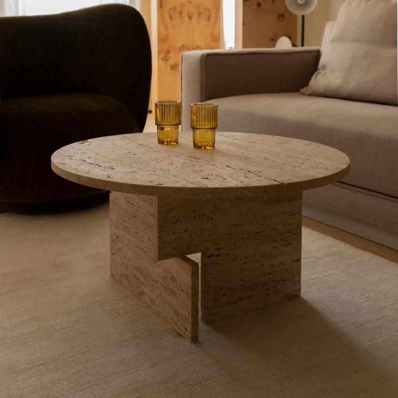 Round pale stone coffee table with intersecting slab supports beside a sofa