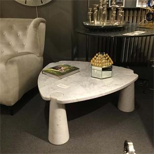 Pale stone coffee table with a curved notched top and tapered legs beside an armchair