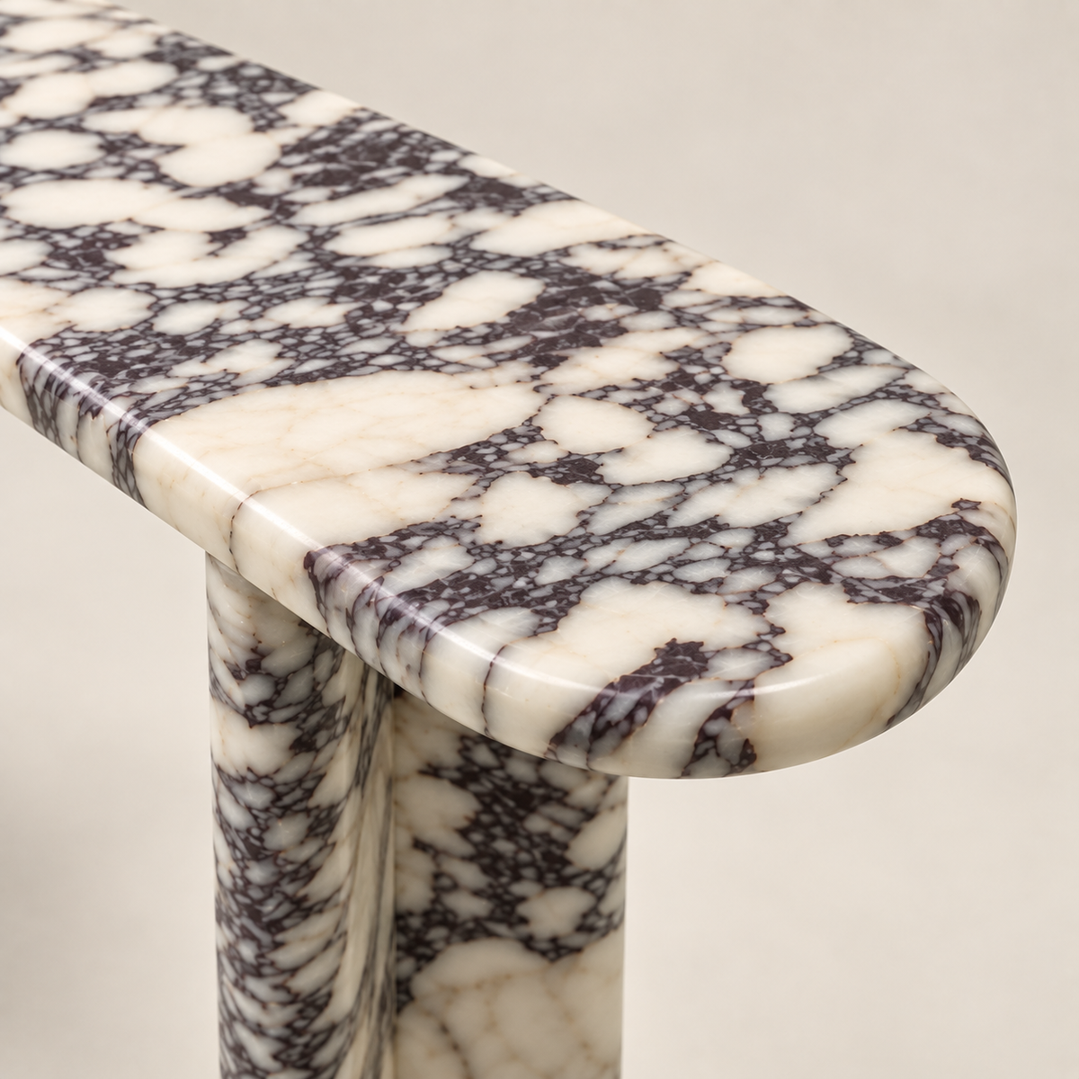 Close-up of the Viola marble console table showing the polished rounded edge, Calacatta Viola veining and part of the stone support.